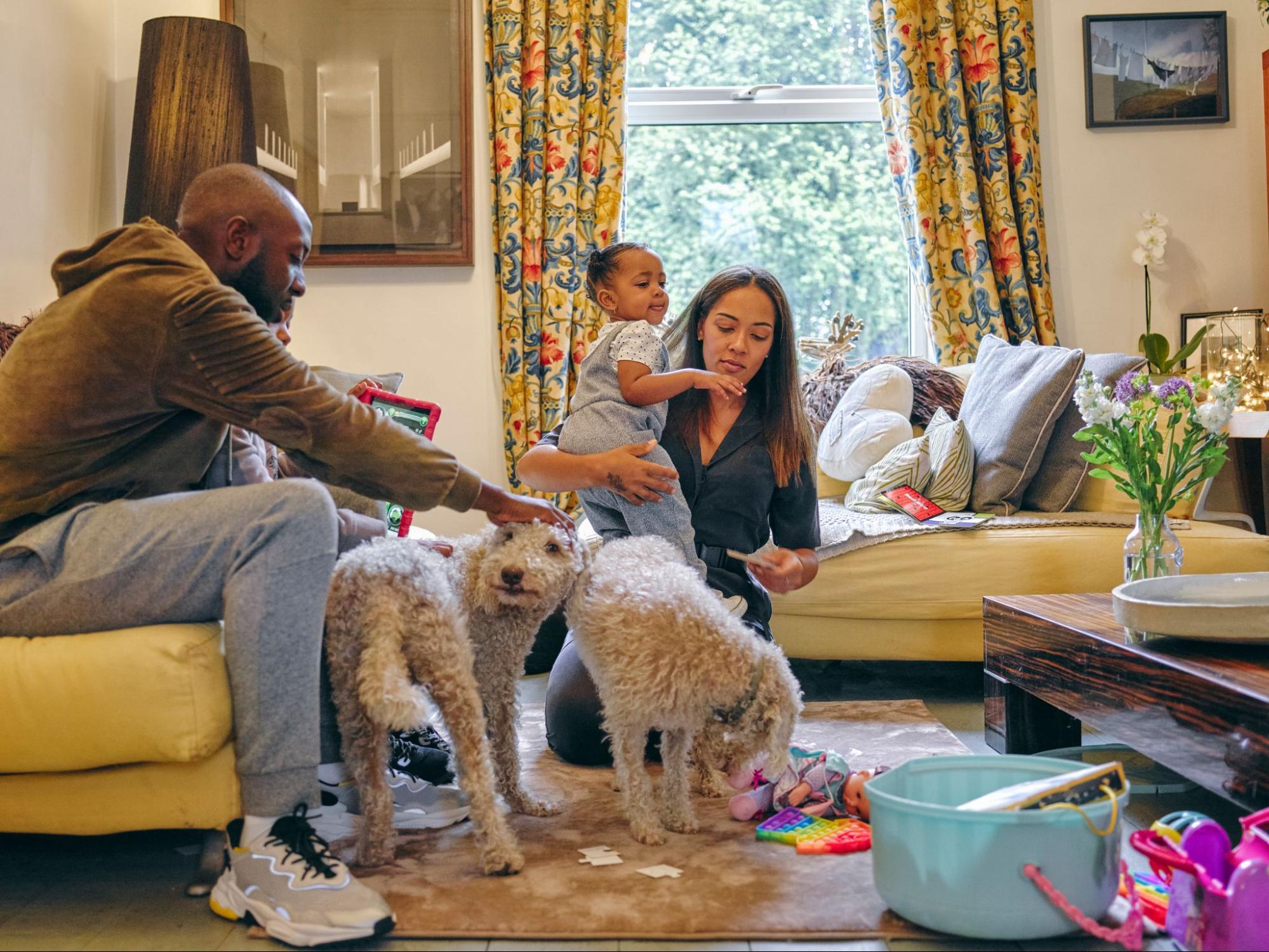 Uma família em uma sala com pets, sofás e tapetes.