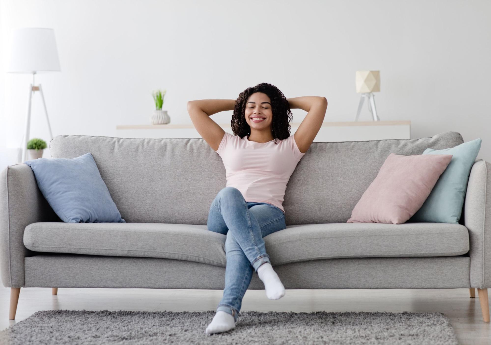 Uma moça sentada em um sofá relaxando com um semblante feliz.