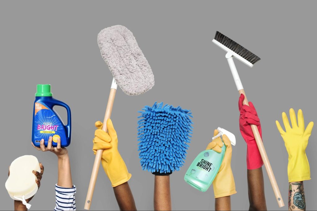 Várias mãos diferentes com utensílios de limpeza, como esponjas, vassouras, luvas, etc.