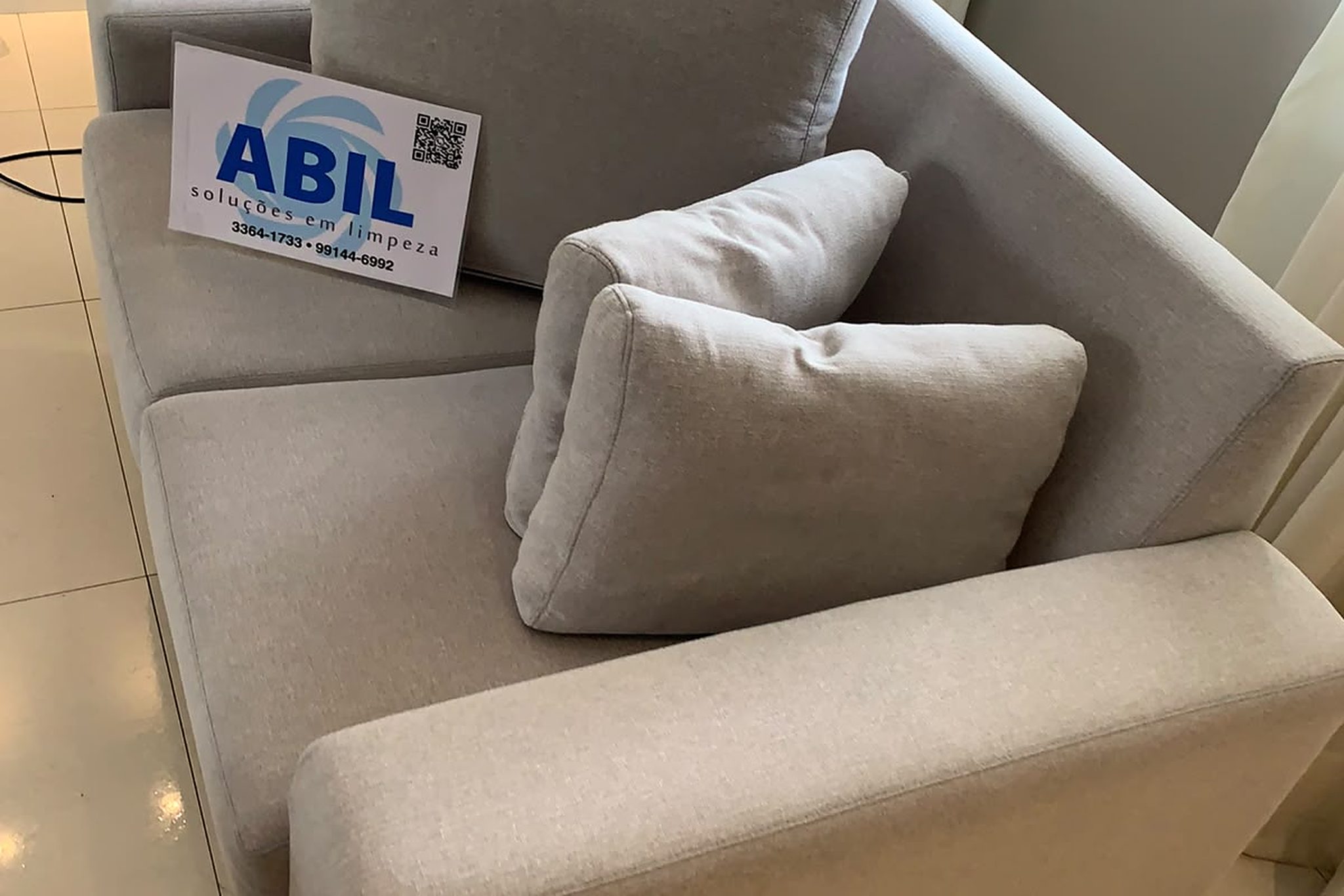 Sofá de tecido claro higienizado pela Abil em Curitiba, com a placa da empresa