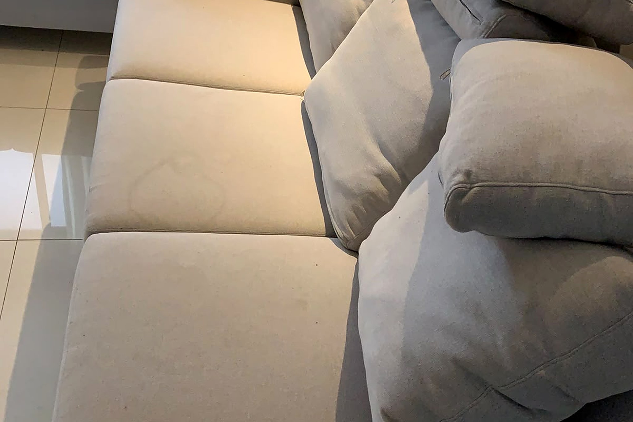 Sofá bege de três lugares com almofadas, aparentemente limpo