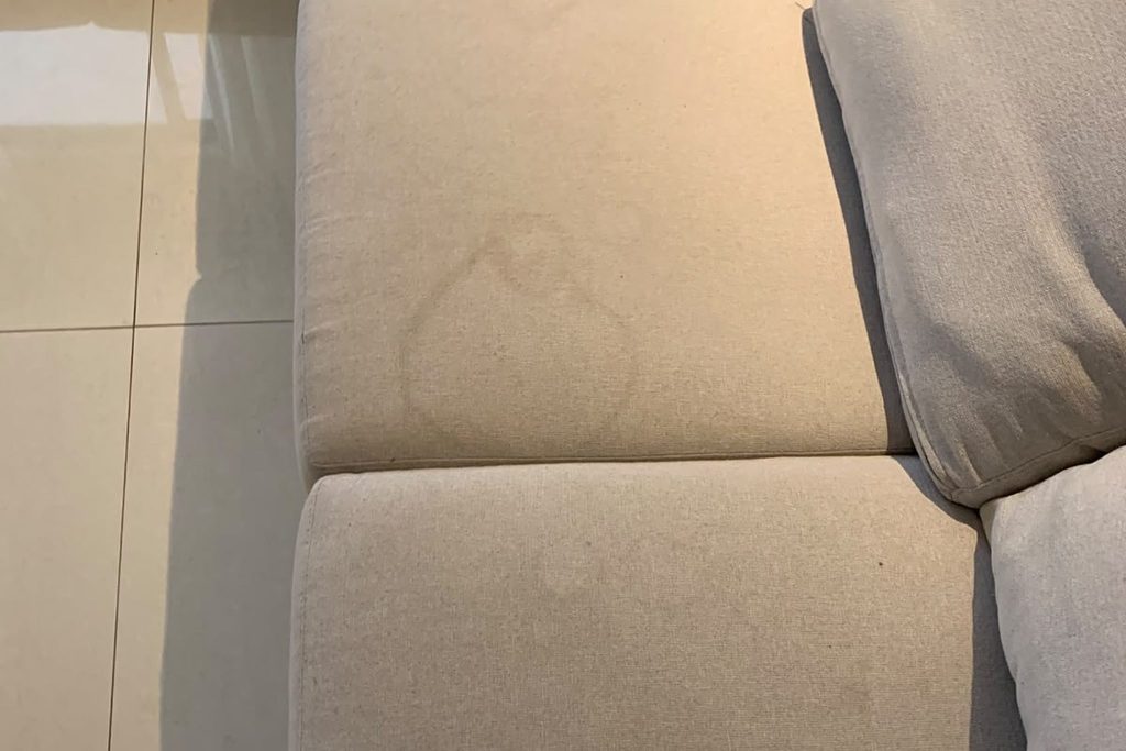 Assento de sofá de tecido claro com marca amarelada de xixi de pet